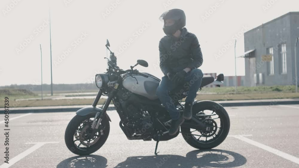 Young attractive motorcyclist with black helmet and black leather jacket on street. Man motorcycle biker Young attractive motorcyclist with black helmet and black leather jacket on street. Man motorcycle biker