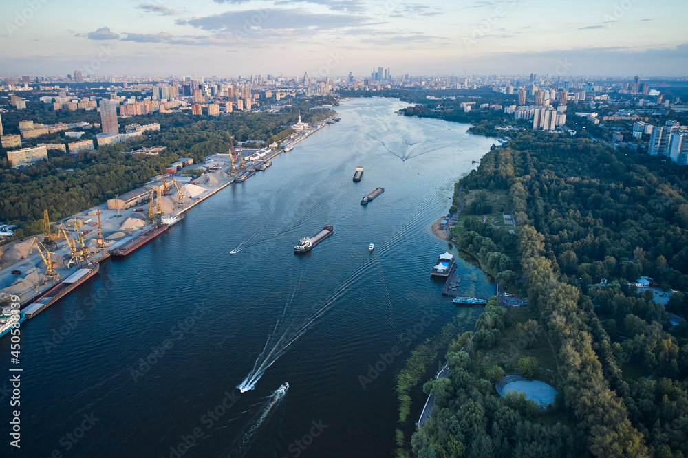 Aerial of ships and vessels are moving through the river in the city. Panoramic view of big city and harbour and public park on the coastlines
