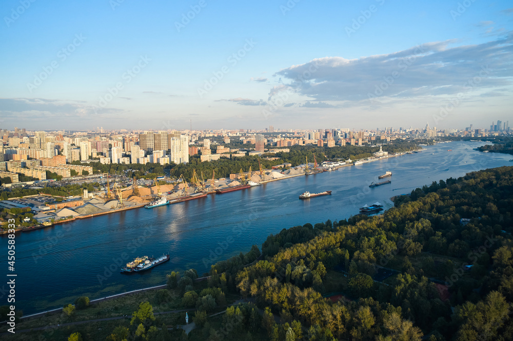 Aerial of ships and vessels are moving through the river in the city. Panoramic view of big city. Harbour and public park on the coastlines. Urban sprawl on the horizon