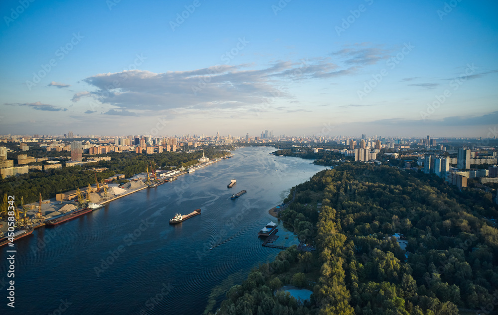 Aerial of ships and vessels are moving through the river in the city. Panoramic view of big city. River port and public park on the coastlines