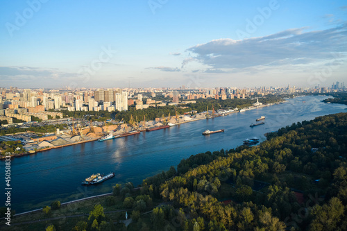 Aerial of ships and vessels are moving through the river in the city. Panoramic view of big city. Harbour and public park on the coastlines. Urban sprawl on the horizon