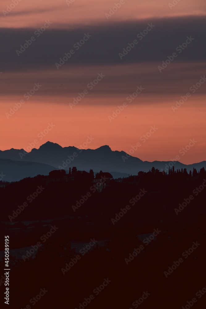 Intense and colored sky during sunset in tuscany, Italy. Mountain silhouettes in the distance, red and orange sky, amazing views of the most famous countryside.