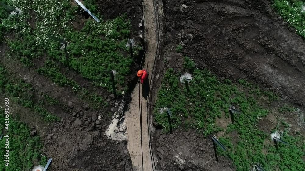 Top view of a worker dragging a cable across the trench at a construction site Top view of a worker dragging a cable across the trench at a construction site