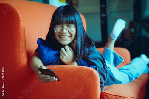 asian teenager holding smartphone lying on sofa at home living room photo