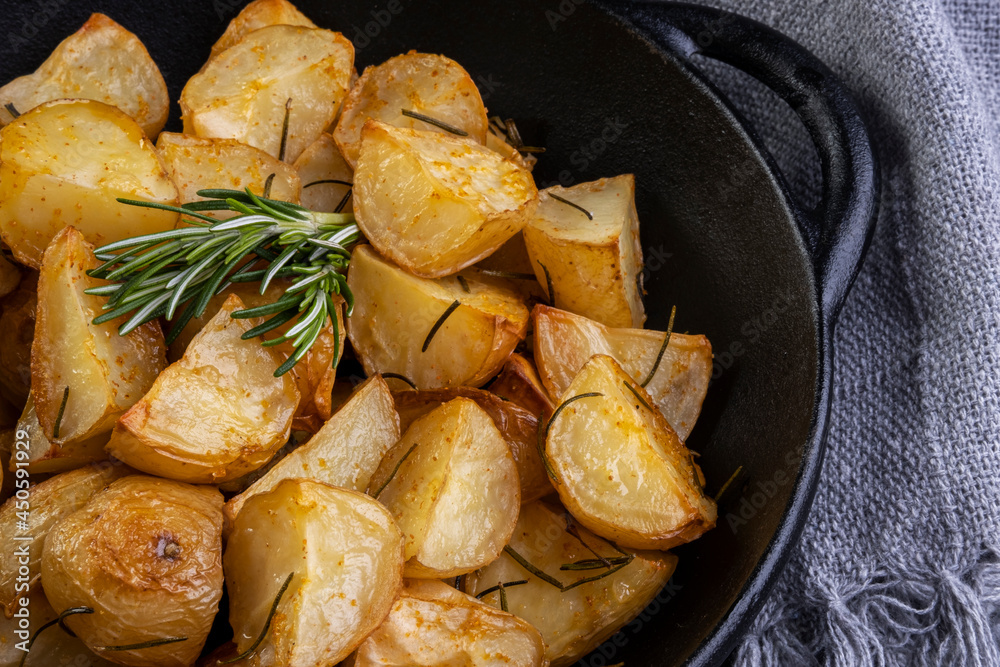 baked fried potatoes with rosemary, coarse salt, olive oil and spice paprika in iron skillet