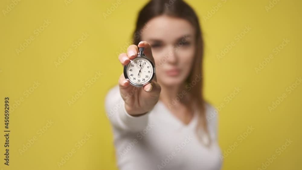 Stopwatch in foreground in hand of attractive young woman. stopwatch counts down from zero. Retro old vintage clock timer in hand of nice lady. little time left, clock is ticking. Yellow background