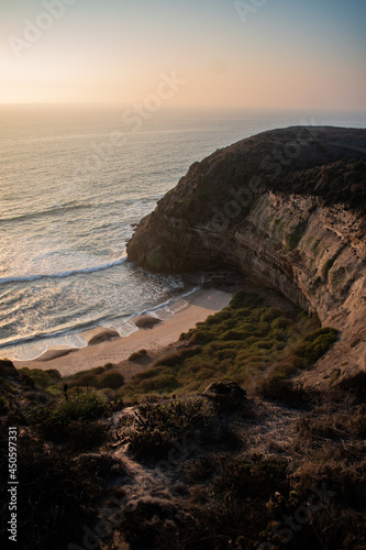 A beautiful beach between cliffs, with green shrubbery, at sunset