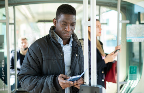 African man browsing on his smartphone while traveling on modern city tram on winter day