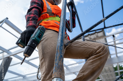 Construction workers wearing safety harness working at high level in the construction site,Roofing tools,Electric drill used on new roofs with Metal Sheet.