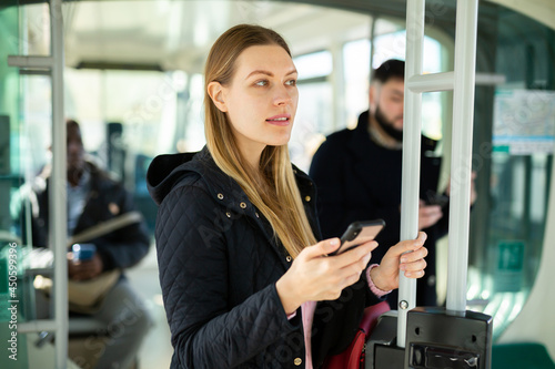 Young focused female passenger browsing on her smartphone during usual trip in public transport