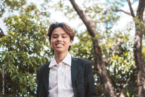 A happy teenage man of Filipino or Pacific Islander descent. In formal wear or university uniform posing outdoors. photo