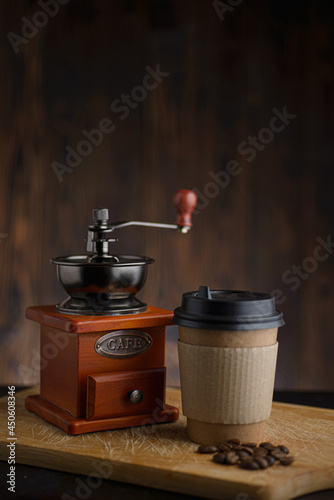 Vintage manual coffee grinder with paper coffee cup on wooden table.