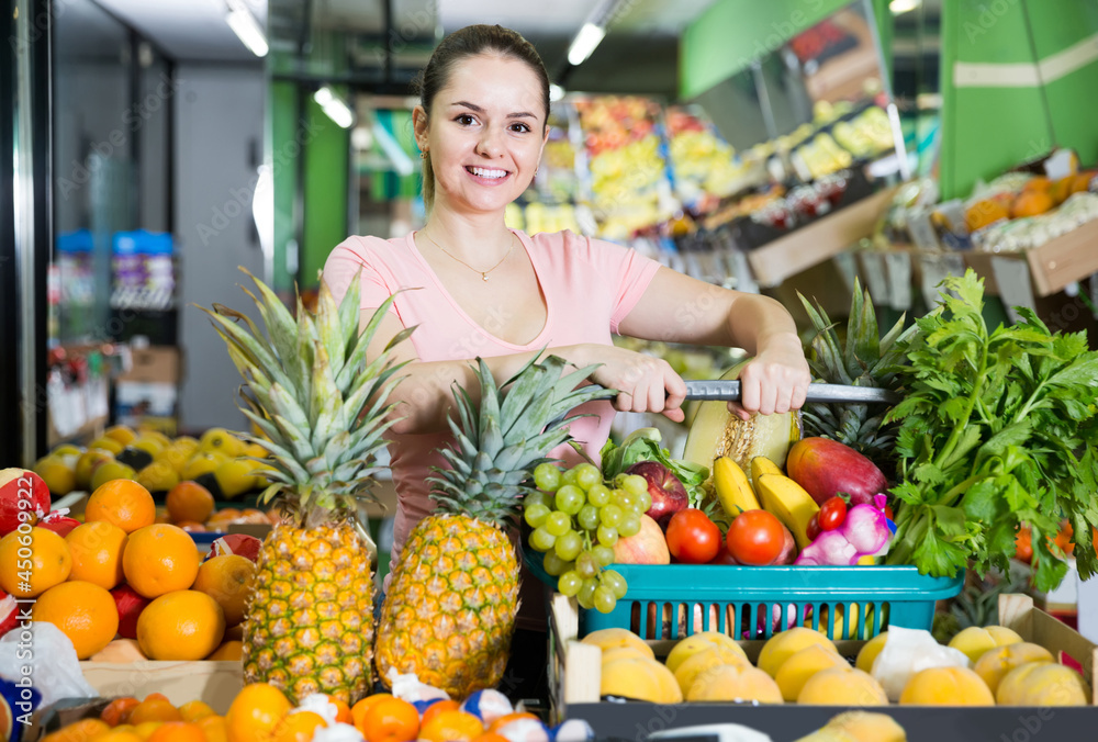 Young french woman with basket with fresh greengrocery enjoying purchases in vegetable store
