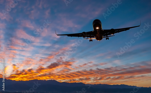 Landing airplane at colorful sunrise with with beams of sun lights. Concept of transport, weather, travel and happy vacation