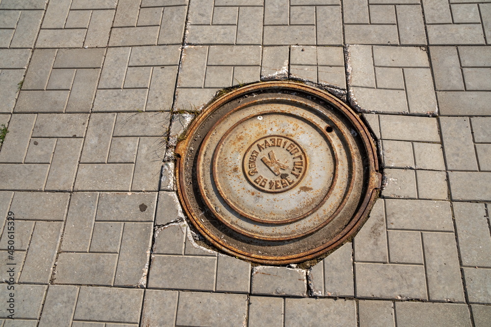 A cast iron manhole cover is located on the pavement of gray concrete tiles.