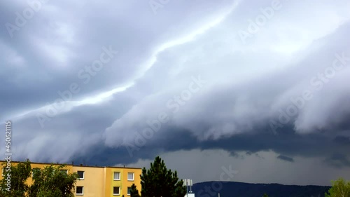 A massive Shelf cloud, Arcus cloud, is slowly moving over the city Usti nad Labem with a lightning strike in the back above the hill