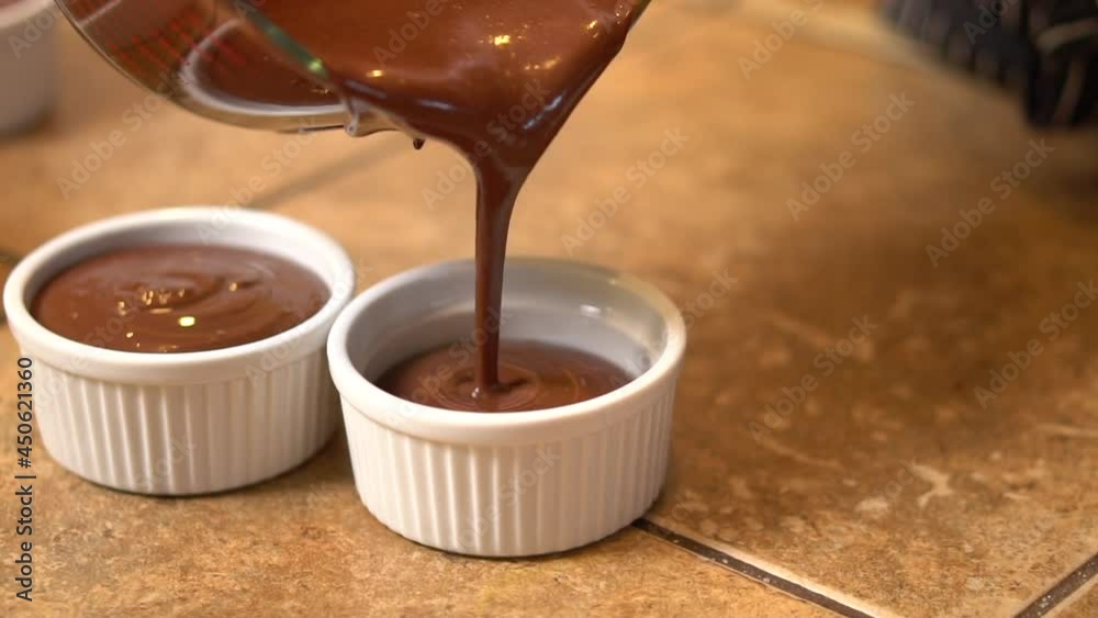 Pouring individual homemade portions of chocolate pot de crème into individual serving cups - slow motion