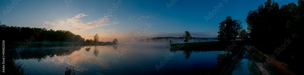 Obraz premium Panorama of the evening lake with a swan and the sun, colorful shades in the sky.