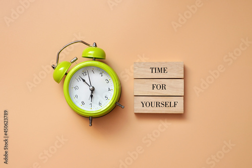 A green alarm clock and the inscription: time for yourself. A symbol of the need to devote time to yourself