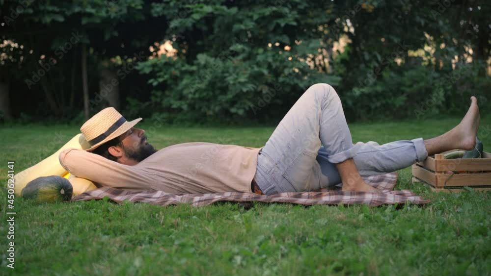 Side view of young male farmer sleeping lying on green meadow with harvest. Wide shot of tired Caucasian man taking a nap outdoors on sunny autumn day. Agriculture and harvesting concept Side view of young male farmer sleeping lying on green meadow with harvest. Wide shot of tired Caucasian man taking a nap outdoors on sunny autumn day. Agriculture and harvesting concept