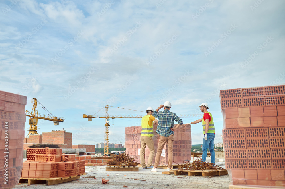 Three workers in hardhats checking the quality of red bricks