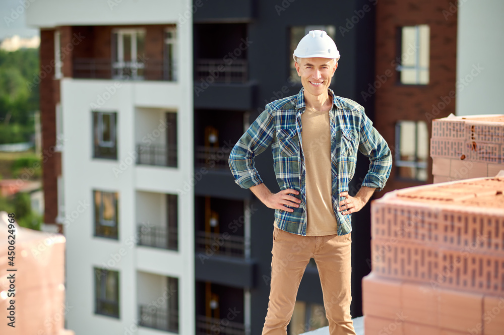 Joyous attractive worker in a hardhat atop a half-constructed building
