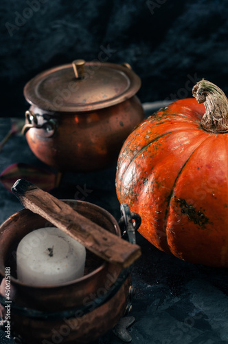 One pumpkin squash and copper or brass witch pots with candles and palo santo incence on the dark black blue textured copy space background halloween holidays concept witchy magic dark moody shot