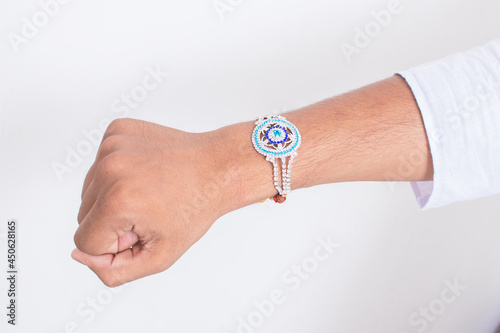 Hand wearing beautiful blue diamond design rakhi on the occasion of raksha bandhan over white background. Indian festival celebrated in India to express love and bond between brother and sister.