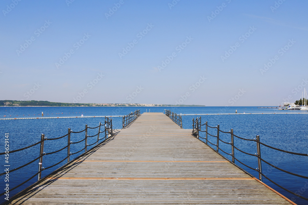The pier near beach against blue sky in sunny day. Adriatic coast and sea in Slovenia. Holiday and travel concept. 