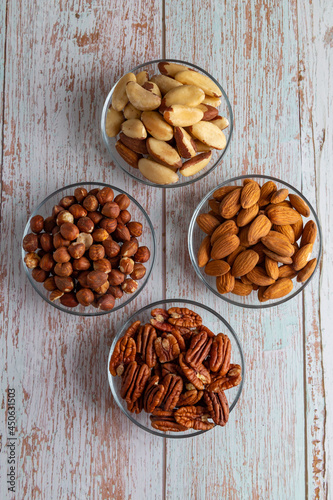 Four types of nuts in four glass bowls on a wooden table, healthy fat and protein food, vegan, ketogenic diet.