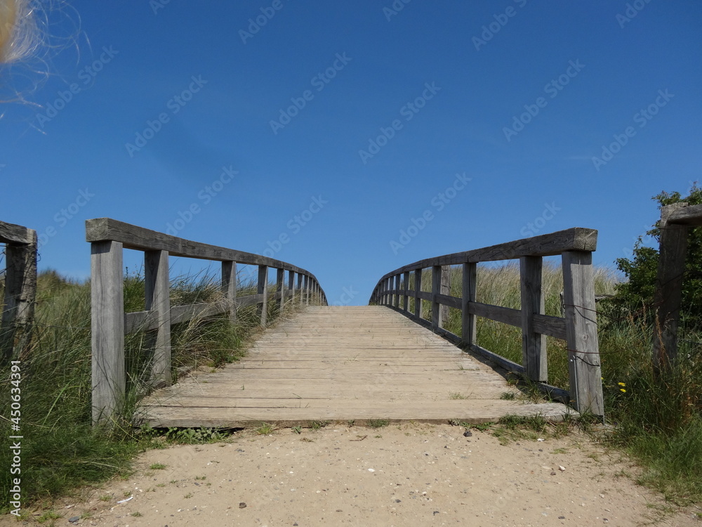 Holzbrücke auf dem Weg zum Meer mit blauem Himmel