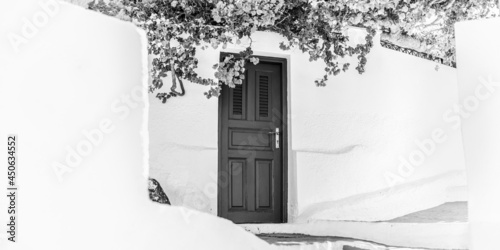 Fototapeta Naklejka Na Ścianę i Meble -  Old door on Santorini island, Greece. Black and white artistic travel scenery, white architecture with flowers and door. Abstract idyllic urban street detail.