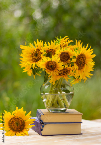 bouquet of beautiful yellow sunflower flowers in a glass vase on a stack of books on a table in the garden