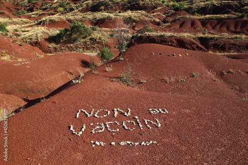 SALAGOU, FRANCE, August 2, 2021: on the red soil of Lake Salagou's shores, activists have used pebbles to write a hostile message regarding vaccination against covid 19. photo