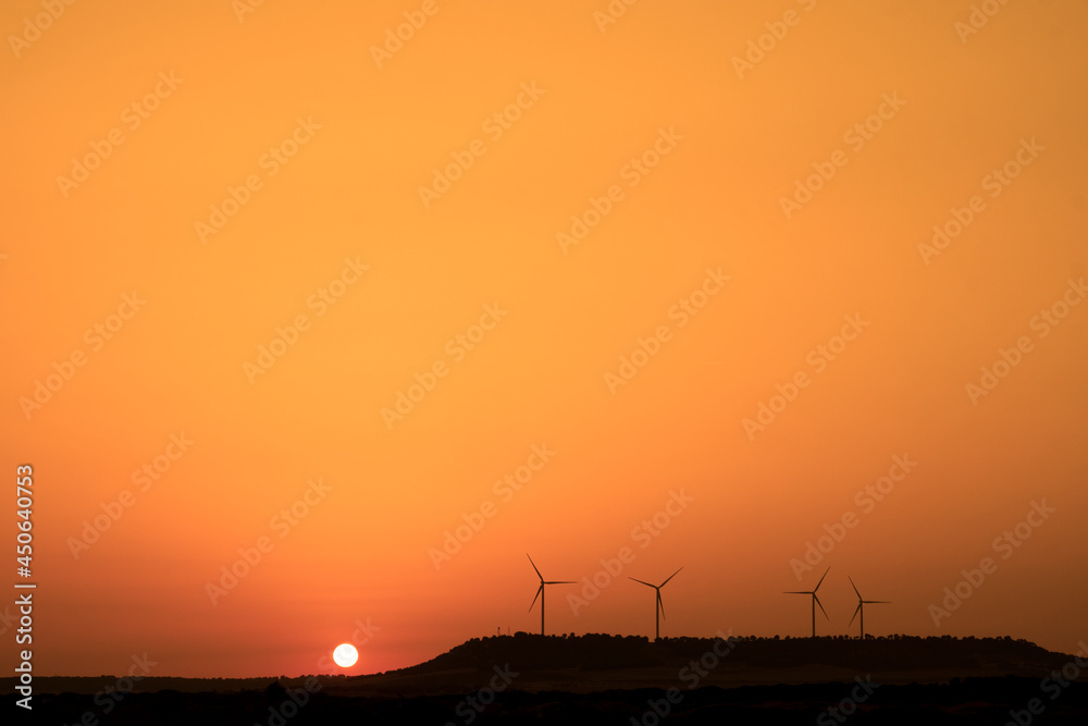 Summer sunset with orange tones over the windmills. Renewable green energy