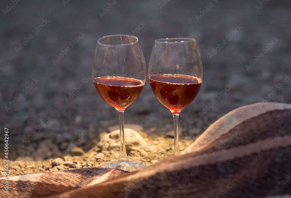 two glasses of red wine are standing on the seashore next to a blanket