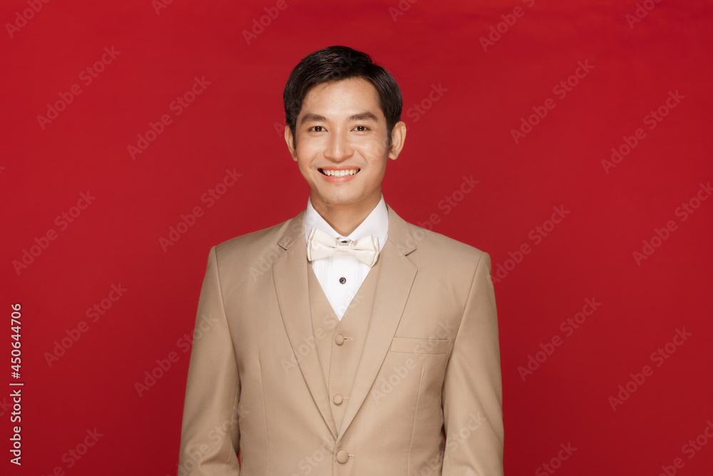 Young attractive Asian man soon to be groom wearing white shirt and beige vest and suit against red background. Concept for pre wedding photography Young attractive Asian man soon to be groom wearing white shirt and beige vest and suit against red background. Concept for pre wedding photography