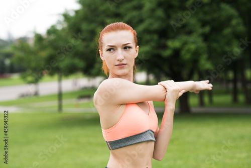 Attractive redhead girl stretching her arm and shoulder in the park