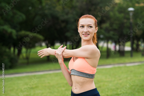 Attractive redhead girl stretching her arm and shoulder in the park © Павел Костенко