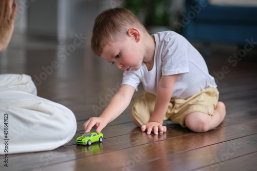 Expressive baby boy playing with a toy car with mother in the background