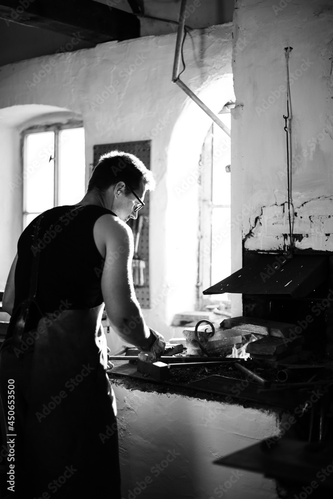 The blacksmith in the production process of metal products handmade in the forge. Black and white photo The blacksmith in the production process of metal products handmade in the forge. Black and white photo