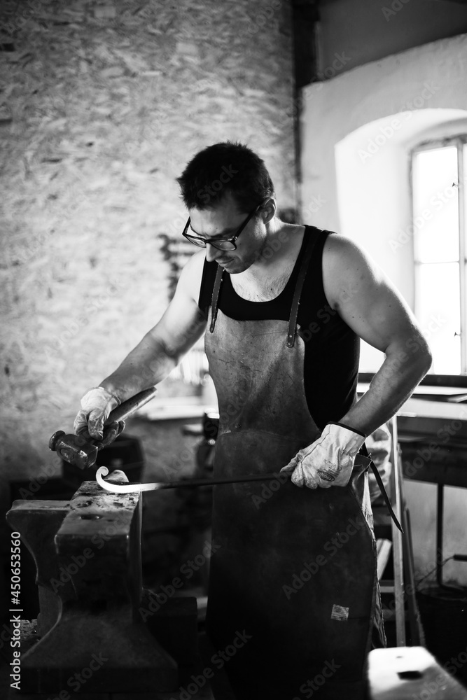 Obraz premium The blacksmith in the production process of metal products handmade in the forge. Blacksmith forging metal with a hammer. Black and white photo