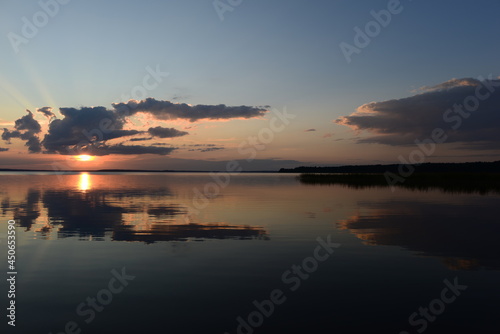 Bright sun rays from the clouds at sunset are reflected in the tranquil water of the lake