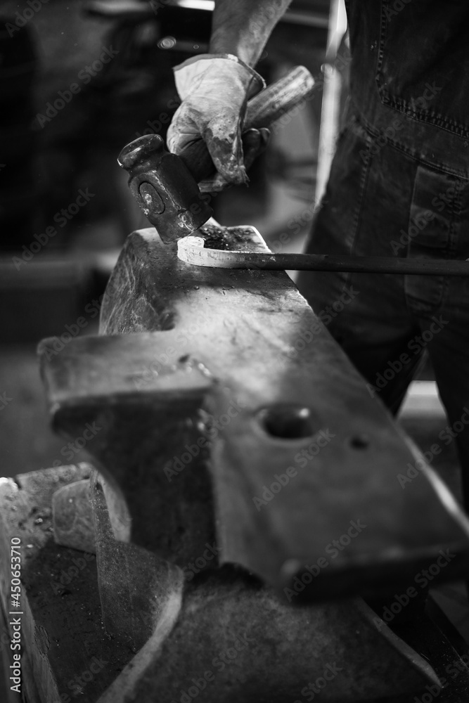 The blacksmith in the production process of metal products handmade in the forge. Blacksmith forging metal with a hammer. Black and white photo