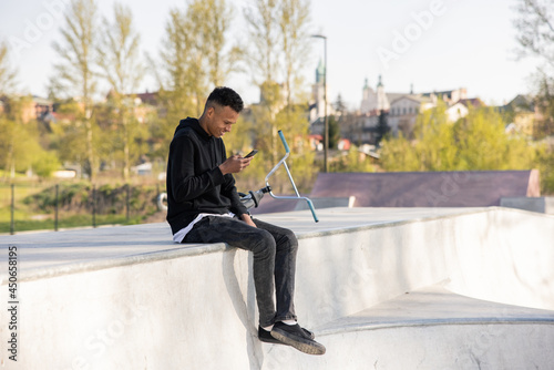 Guy sits in helmet with bmx bike in park on ramp, at skatepark with phone in hand and texts friends he hangs out with to do tricks photo