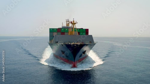 Front view of a loaded container cargo vessel traveling with speed over blue ocean