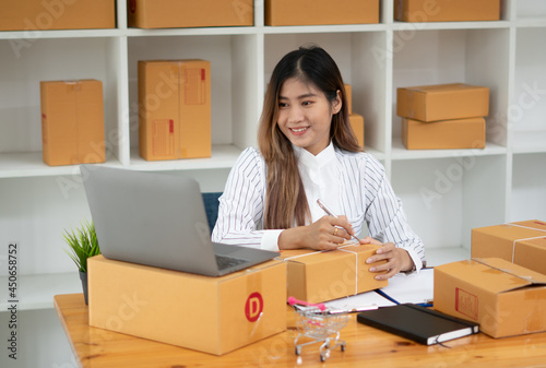 Startup small business entrepreneur SME, young asian woman working with laptop computer and delivery packaging box, online market packing, SME e-commerce seller concept.