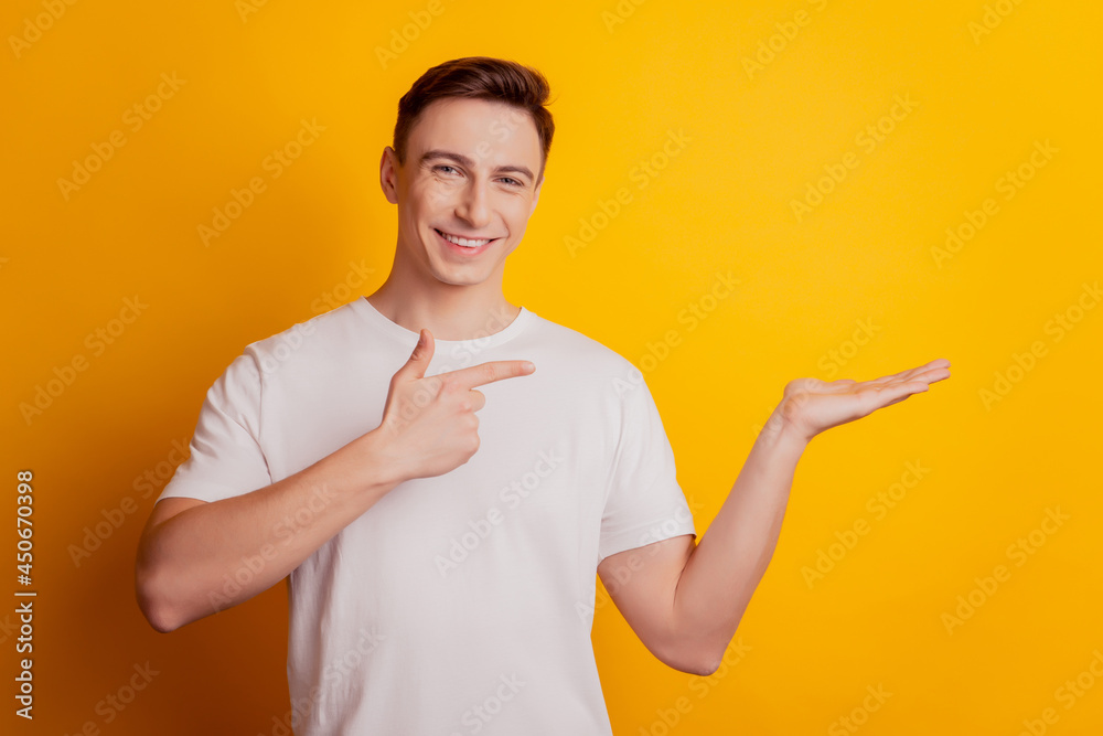 Portrait of charming guy palm hold blank space indicate forefinger on yellow background