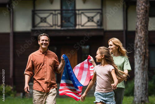 Smiling man holding american flag near wife and daughter outdoors