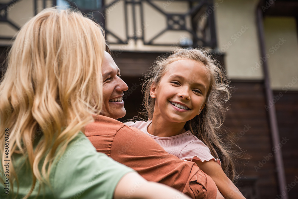 Man hugging smiling kid near blurred wife outdoors